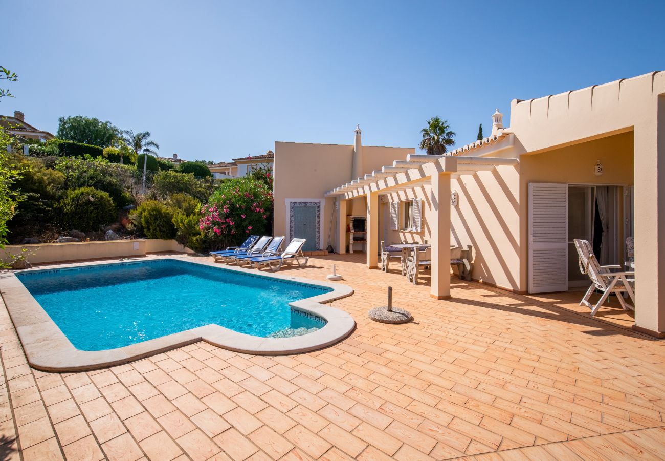 Sunny terrace with pool and dining area at a holiday home. Sunny terrace with pool and dining area under a pergola next to a house under a clear blue sky.