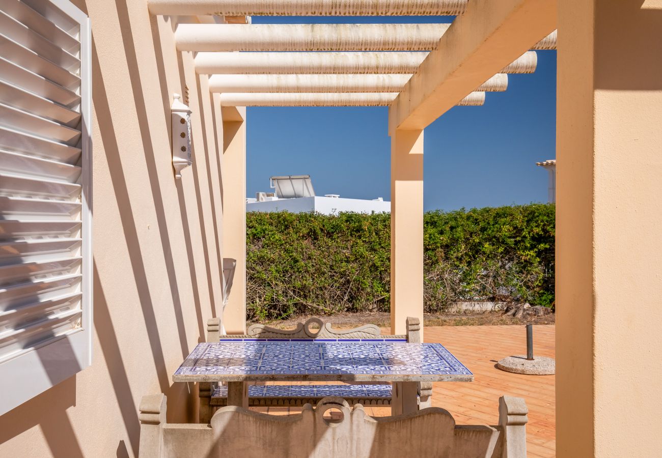 Sunny covered terrace with a tiled table and benches. Table and benches with blue and white tiles under a pergola on a sunny terrace.