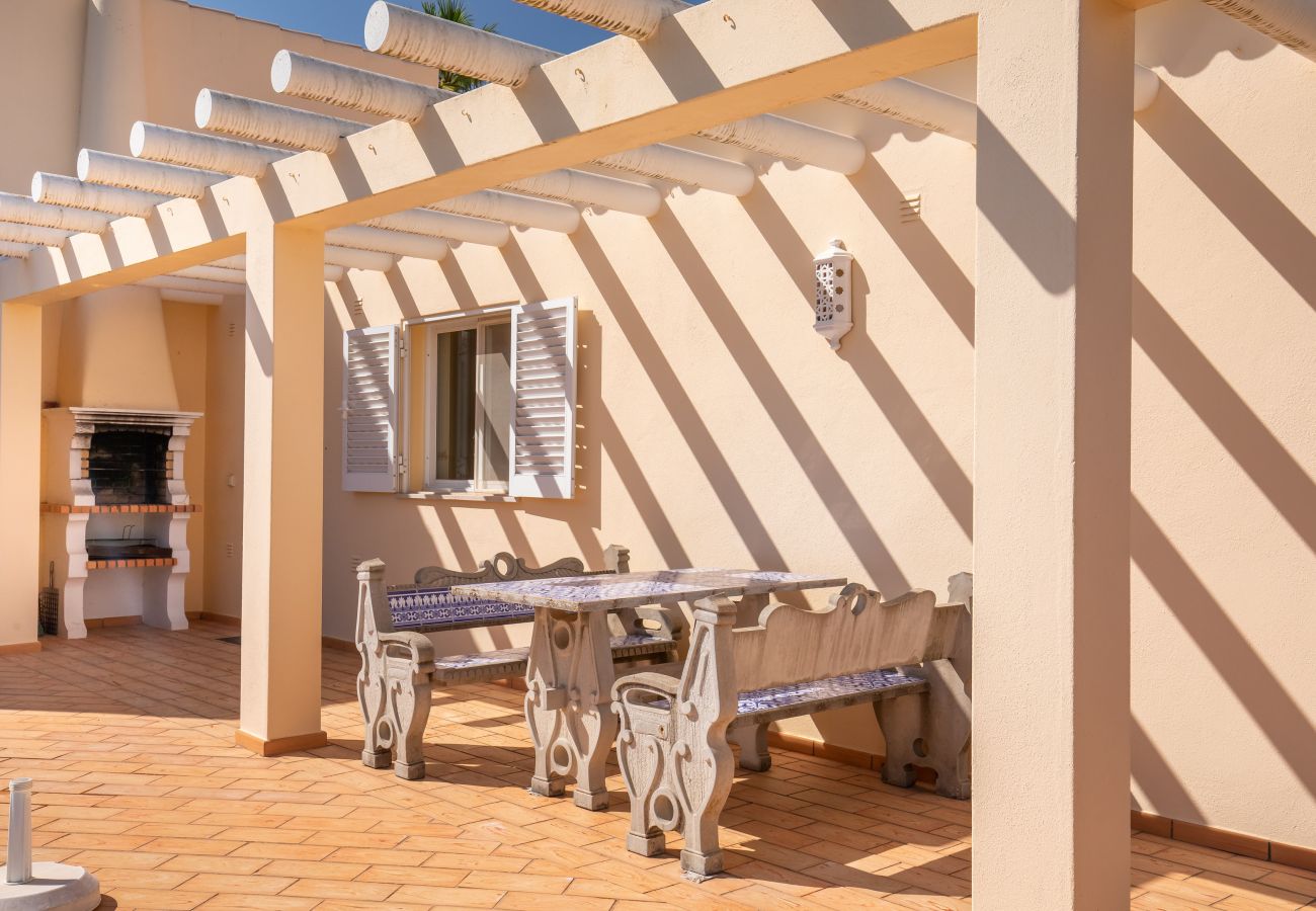 Barbecue area on the terrace with a built-in grill and seating. Built-in barbecue area with a table and benches under a pergola on a sunny terrace.