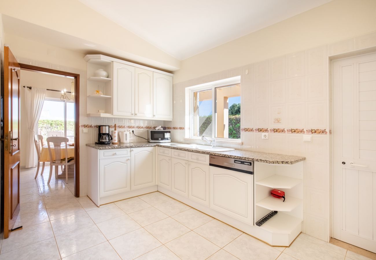 Bright, modern kitchen with white cabinets and a window. Interior of a white kitchen with a counter, sink, and view into an adjacent dining room.