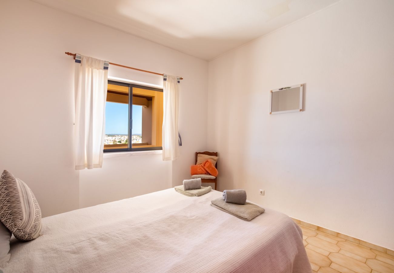 Small, Cozy Bedroom with Double Bed and Color Accents Cozy bedroom with a double bed, beige tiled floor, wall mirror, window with light curtains, and a wooden chair.