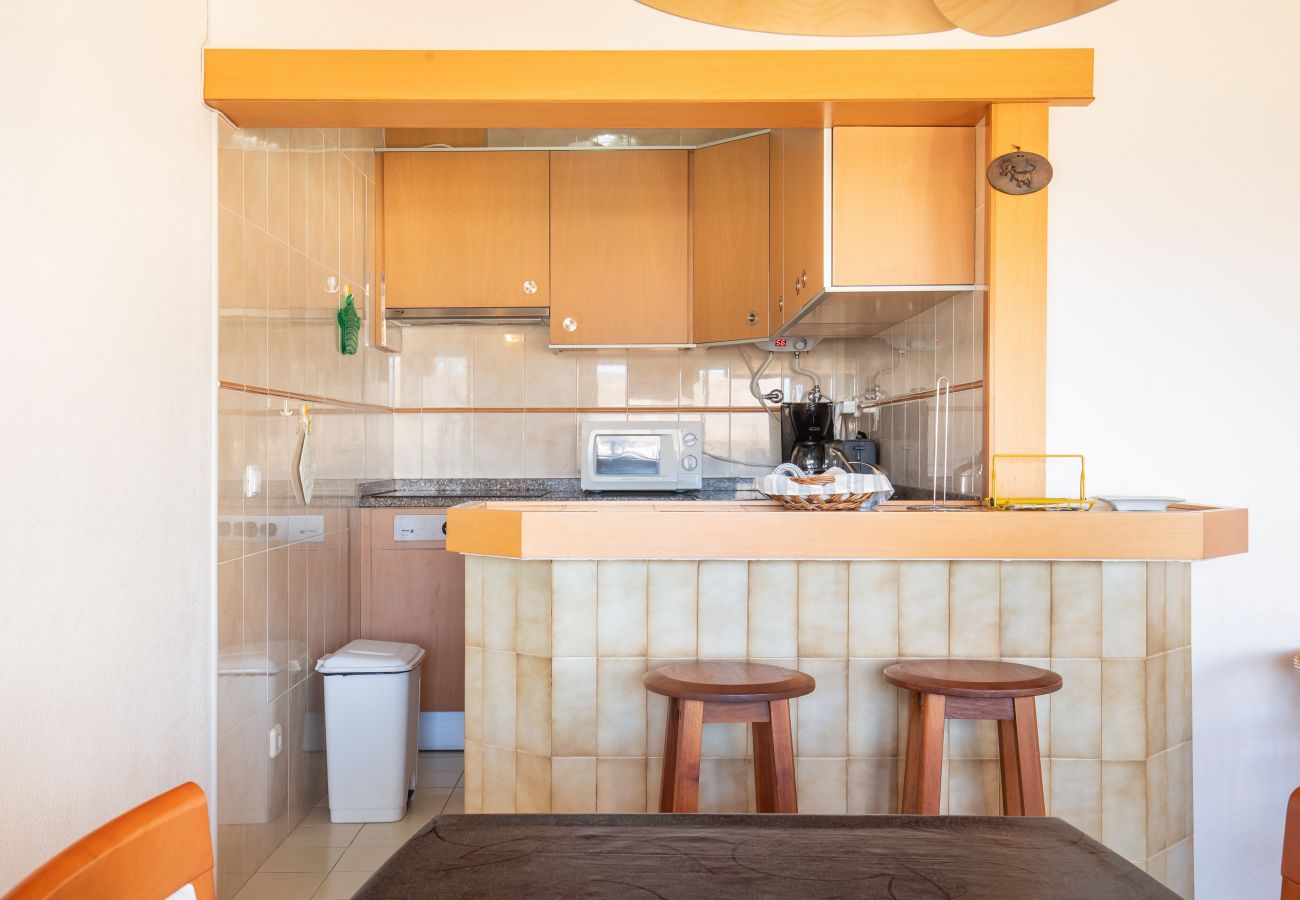 Bright Kitchenette and Bar with Wooden Counter in Mediterranean Style Kitchenette with beige tiles, light wood cabinets, a bar with a wooden counter, and two simple wooden bar stools.