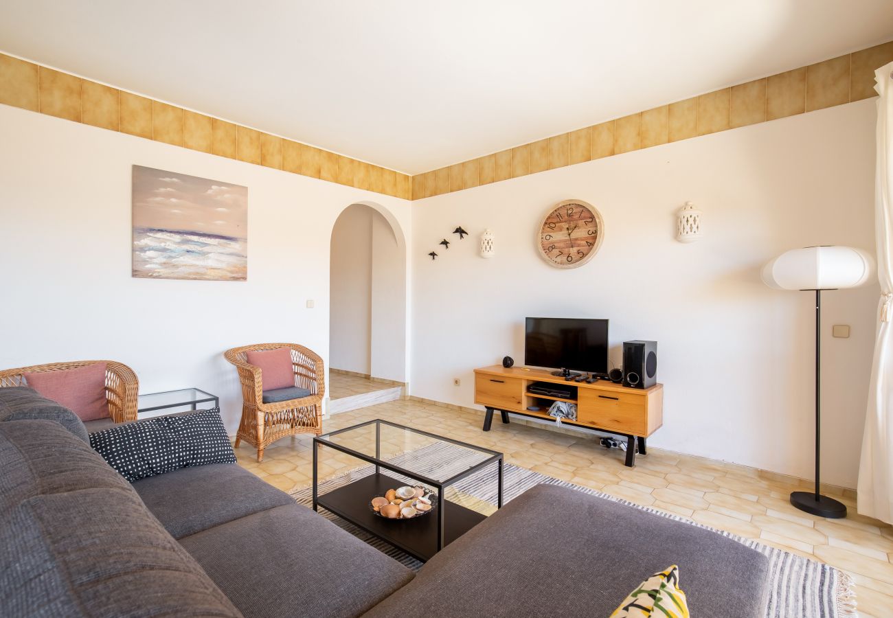 Cozy Living Room with Sofa, Rattan Chairs, and Mediterranean Border Bright living room with a grey sectional sofa, glass table, two rattan chairs, wooden TV stand, and yellow tiled border.