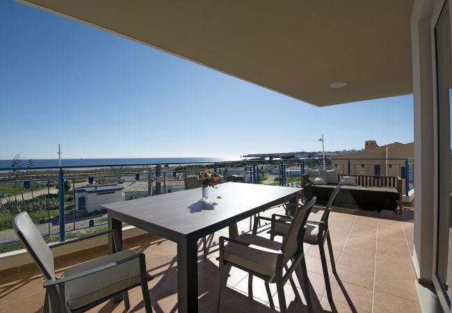 Terraço parcialmente coberto da Casa Areia Ornata com vista magnífica para a praia e o mar e mesa de jantar e banco estofado