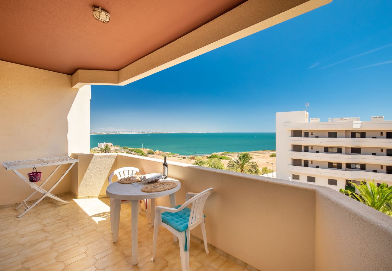 Varanda mobilada com vista desimpedida para o mar azul-turquesa e costa sob um céu azul.