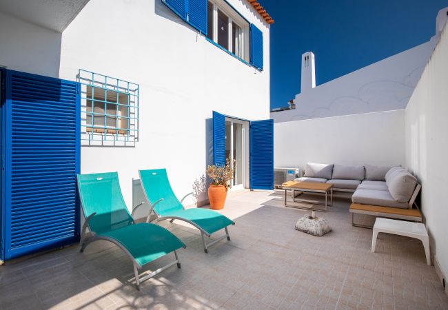 Pátio com Área de Lounge e Espreguiçadeiras Pátio com sofá branco, mesa de madeira, espreguiçadeiras turquesa e portadas azuis.