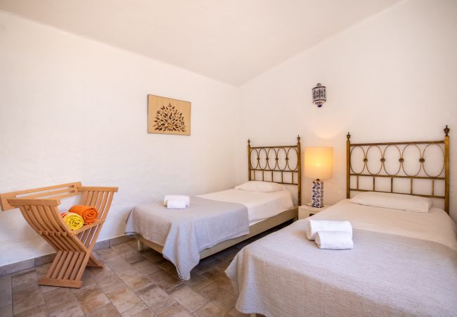 Quarto com duas camas de solteiro e charme rústico Quarto com duas camas de solteiro, cabeceiras de metal dourado e uma mesa de cabeceira com um candeeiro de azulejos azuis.
