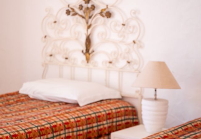 Vista detalhada de um quarto com cabeceira ornamentada Primeiro plano de duas camas de solteiro com colchas xadrez e uma cabeceira de metal branco ornamentada.