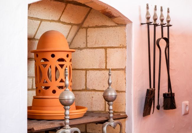 Lareira com vaso de cerâmica e ferramentas de lareira Uma lareira com um vaso de cerâmica laranja, apoios de metal e um conjunto de ferramentas de lareira pendurado na parede.