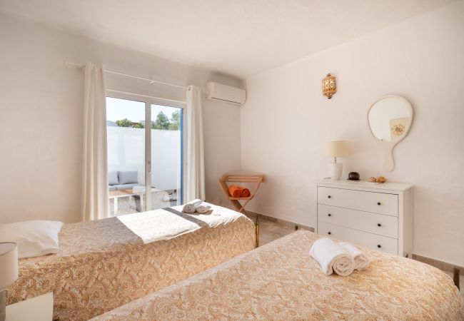 Quarto com Duas Camas de Solteiro e Acesso ao Pátio Quarto com duas camas de solteiro, cómoda branca, espelho redondo e porta de correr para o pátio.