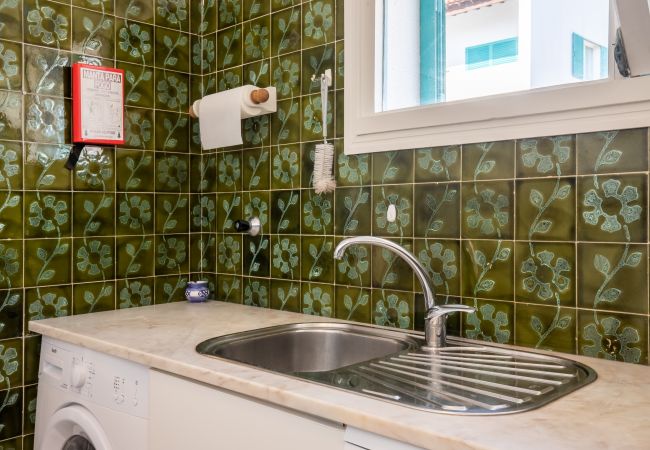 Lava-loiça e Máquina de Lavar Roupa da Cozinha Balcão da cozinha com lava-loiça, máquina de lavar roupa e azulejos verdes.