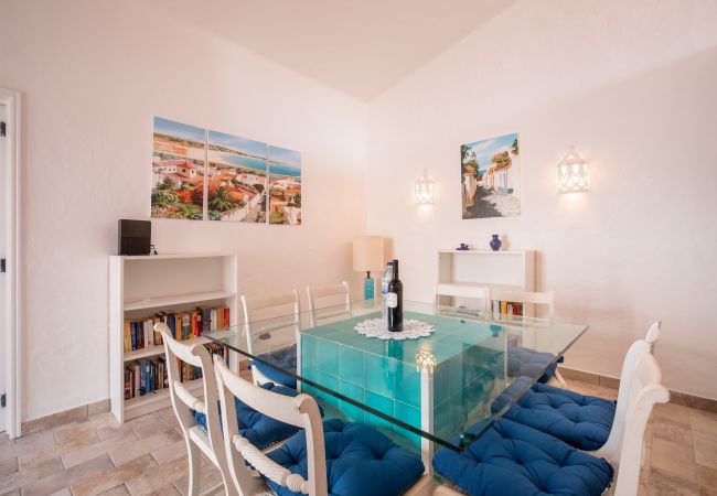 Área de Jantar com Mesa de Vidro e Arte na Parede Área de jantar com mesa de vidro, cadeiras com almofadas azuis e quadros costeiros na parede.