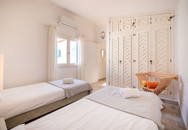 Quarto com Duas Camas e Roupeiro Quarto com duas camas de solteiro, roupeiro embutido branco com padrão de losangos e janela.
