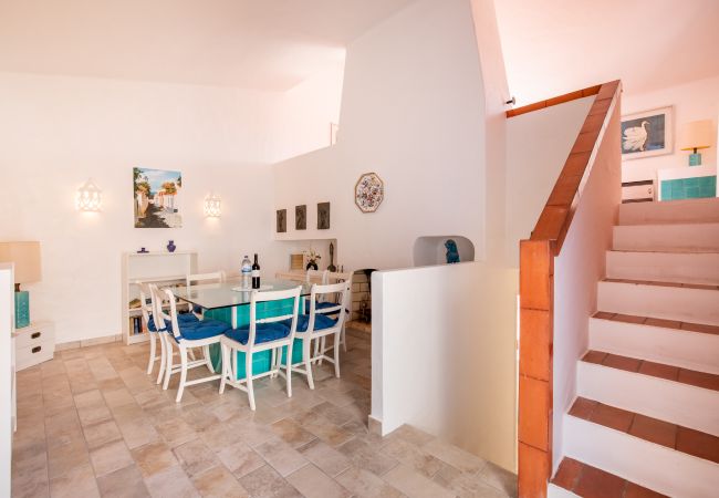 Área de Jantar com Escadaria Área de jantar aberta com mesa de vidro, cadeiras azuis e escadas.