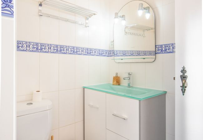 Casa de Banho com Toucador e Espelho Casa de banho com toucador branco, faixa de azulejos azul e branco e azulejos escuros no chão.