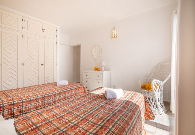 Quarto com Duas Camas de Solteiro e Colchas Xadrez Quarto com duas camas de solteiro, colchas xadrez vermelhas e laranjas, guarda-roupa branco e cômoda.