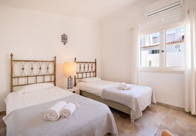 Quarto com Duas Camas de Solteiro e Cabeceiras Douradas Quarto com duas camas de solteiro, cabeceiras douradas, mesa de cabeceira com luminária e janela.