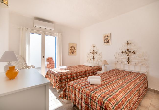 Quarto com Duas Camas de Solteiro e Cabeceiras de Metal Brancas Quarto com duas camas de solteiro, colchas xadrez vermelhas e laranjas, cabeceiras de metal brancas e uma cômoda.