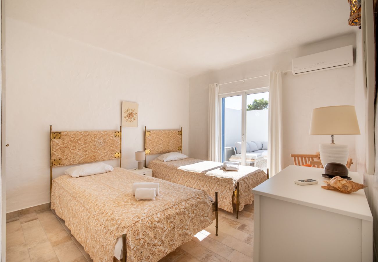 Quarto com Duas Camas de Solteiro e Acesso ao Pátio Quarto com duas camas de solteiro, cabeceiras douradas e cômoda branca, com acesso ao pátio.