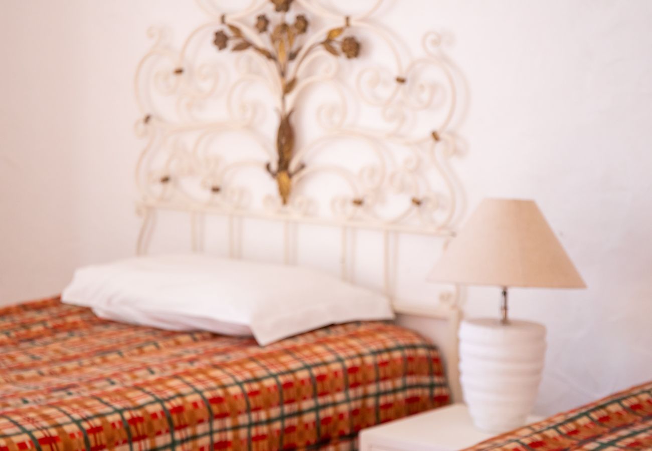 Vista detalhada de um quarto com cabeceira ornamentada Primeiro plano de duas camas de solteiro com colchas xadrez e uma cabeceira de metal branco ornamentada.