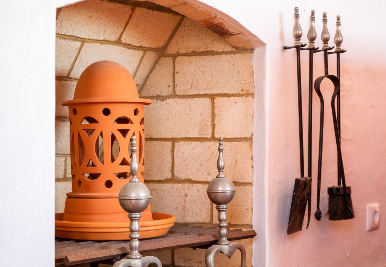 Lareira com vaso de cerâmica e ferramentas de lareira Uma lareira com um vaso de cerâmica laranja, apoios de metal e um conjunto de ferramentas de lareira pendurado na parede.