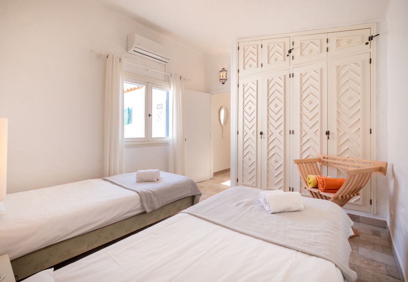 Quarto com Duas Camas e Roupeiro Quarto com duas camas de solteiro, roupeiro embutido branco com padrão de losangos e janela.