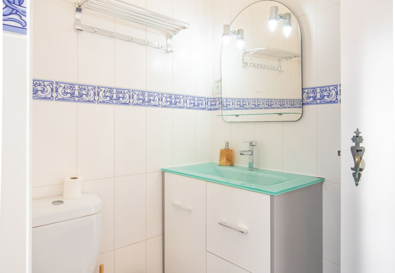Casa de Banho com Toucador e Espelho Casa de banho com toucador branco, faixa de azulejos azul e branco e azulejos escuros no chão.