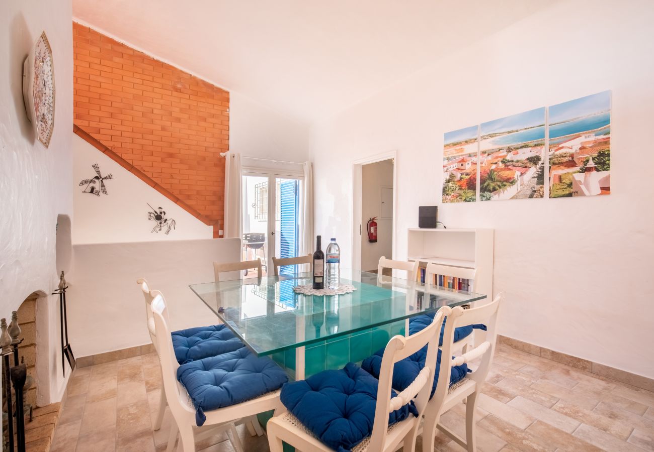 Área de Jantar com Mesa de Vidro e Parede de Tijolo Área de jantar com mesa de vidro, cadeiras azuis, parede de tijolo e quadros costeiros.