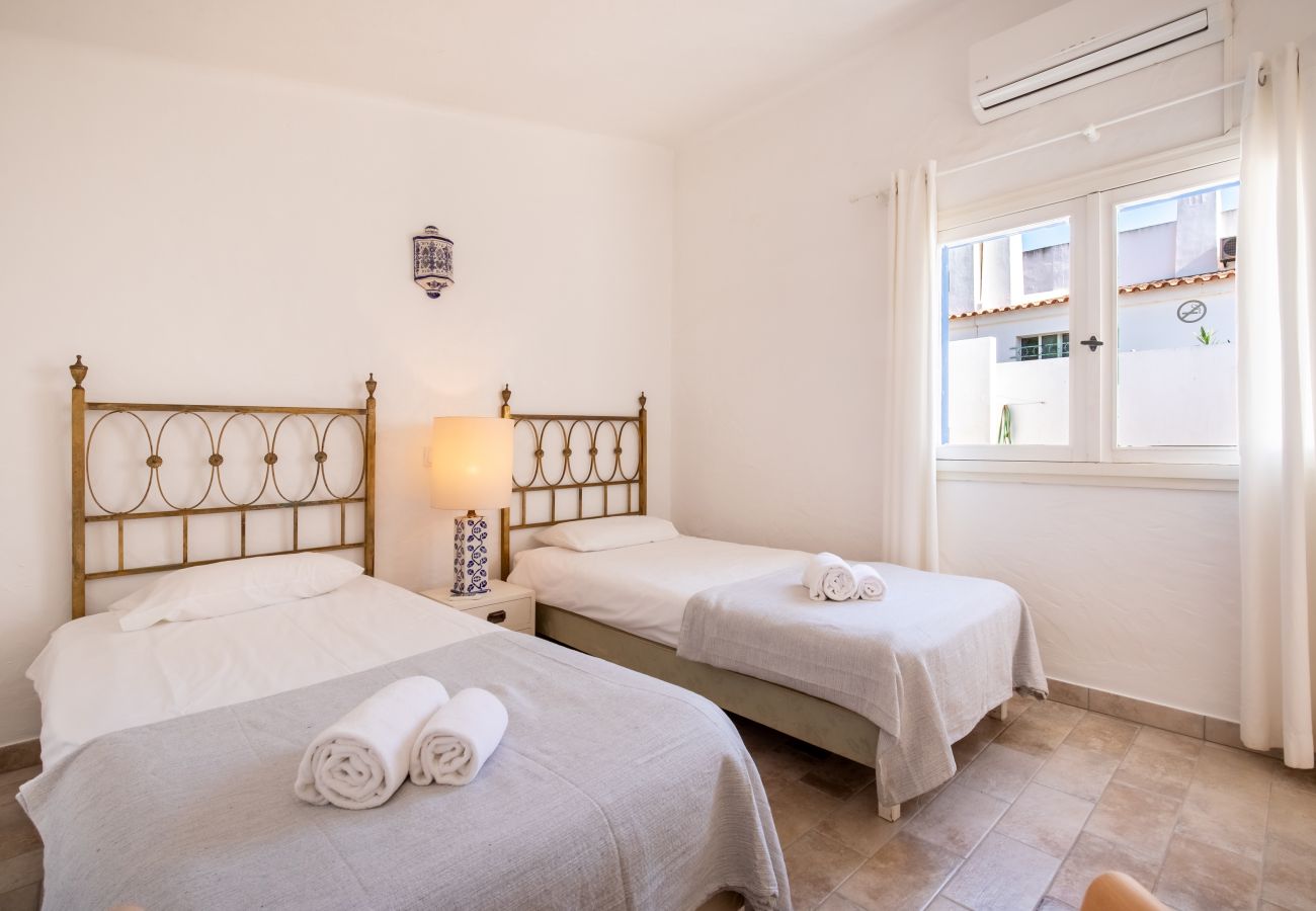 Quarto com Duas Camas de Solteiro e Cabeceiras Douradas Quarto com duas camas de solteiro, cabeceiras douradas, mesa de cabeceira com luminária e janela.