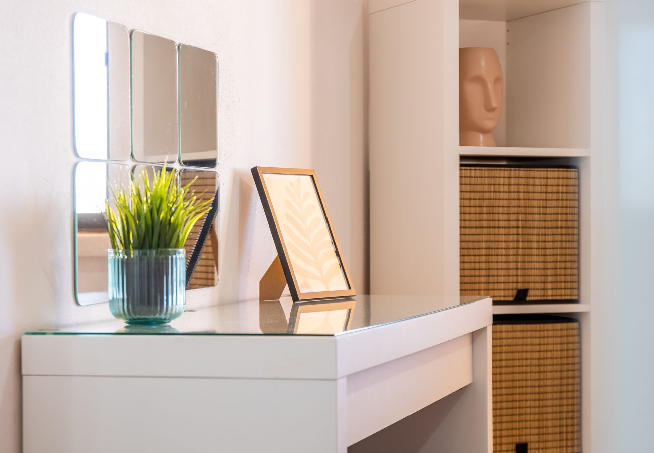 Cantinho de Beleza Moderno e Funcional Secretária branca com espelhos quadrados, plantas e prateleira branca com cestos de vime e cabeça decorativa.