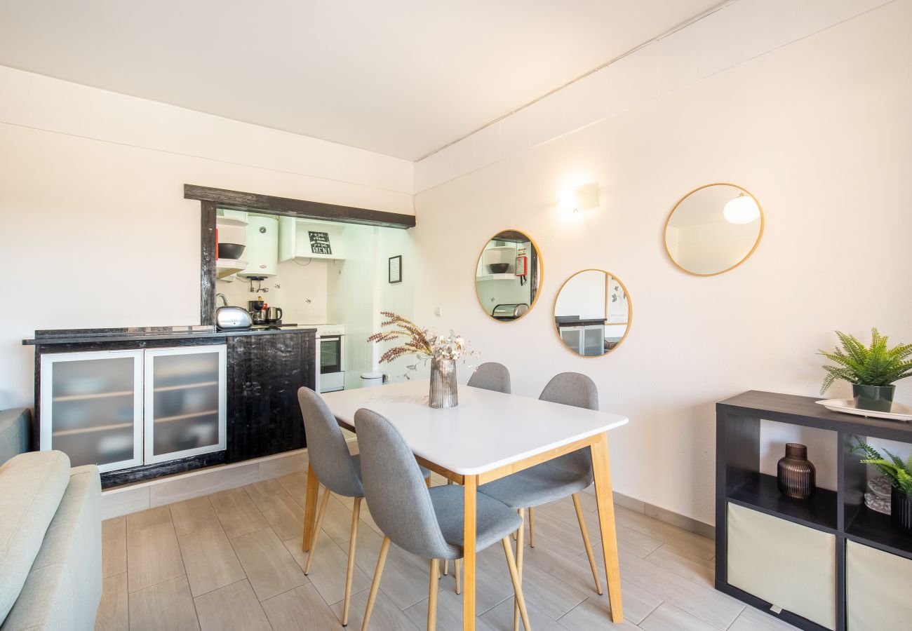 Jantar Moderno com Espelhos Decorativos e Bar Área de jantar com mesa branca, cadeiras cinzentas, espelhos redondos e abertura para a cozinha com bar preto.