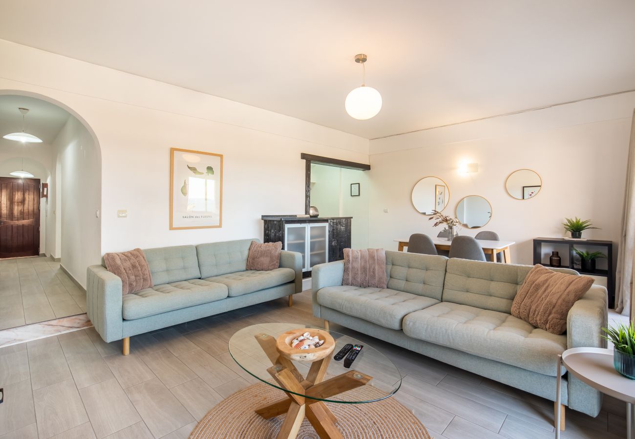 Sala de Estar em Plano Aberto: Conforto e Estilo Moderno Sala de estar clara com dois sofás verde-menta, mesa de centro, área de jantar com espelhos redondos e arco para o corredor.