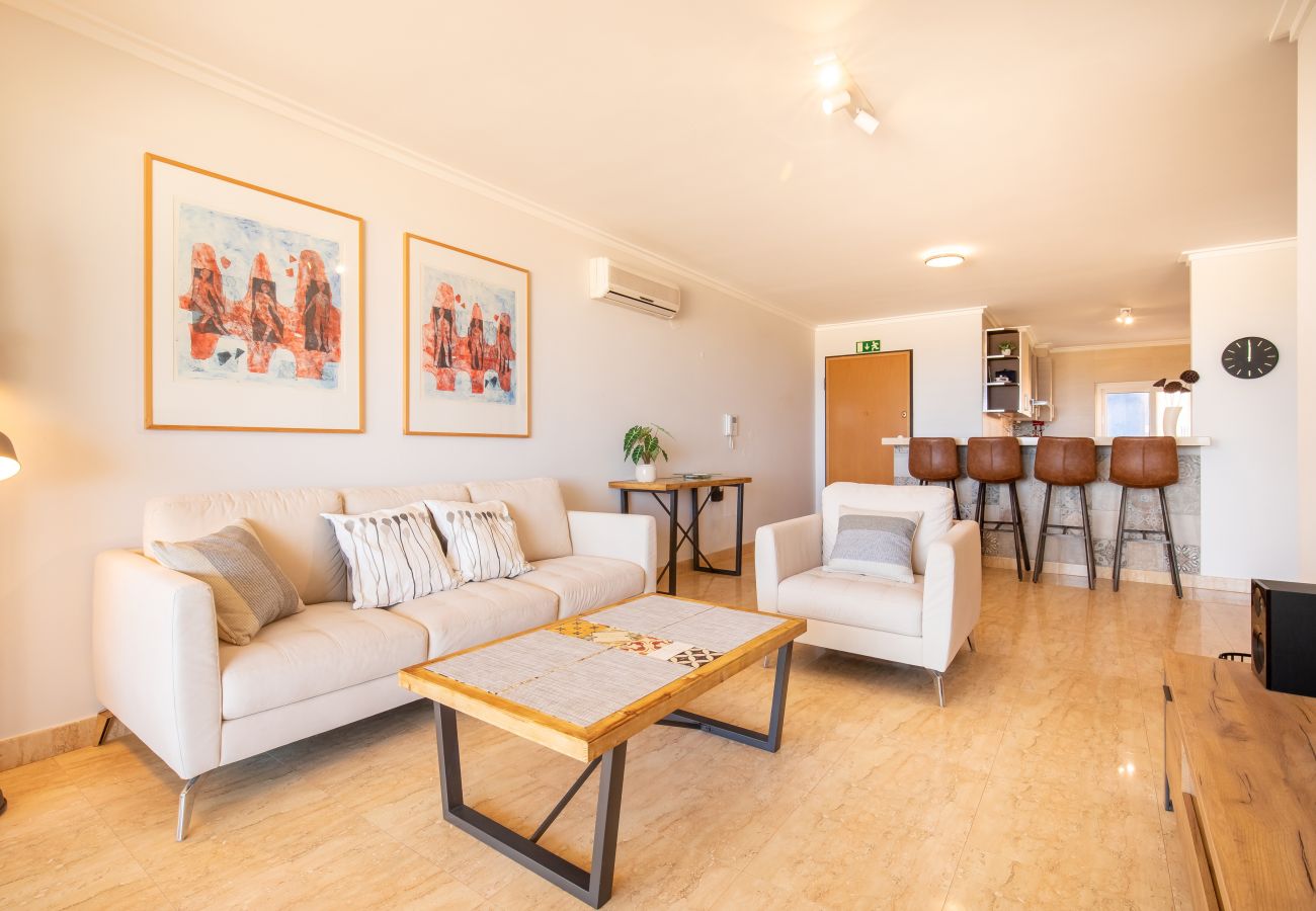 Área de Estar e Jantar em Plano Aberto Uma sala de estar moderna em plano aberto com um sofá creme, mesa de centro e uma vista da área do bar da cozinha ao fundo.