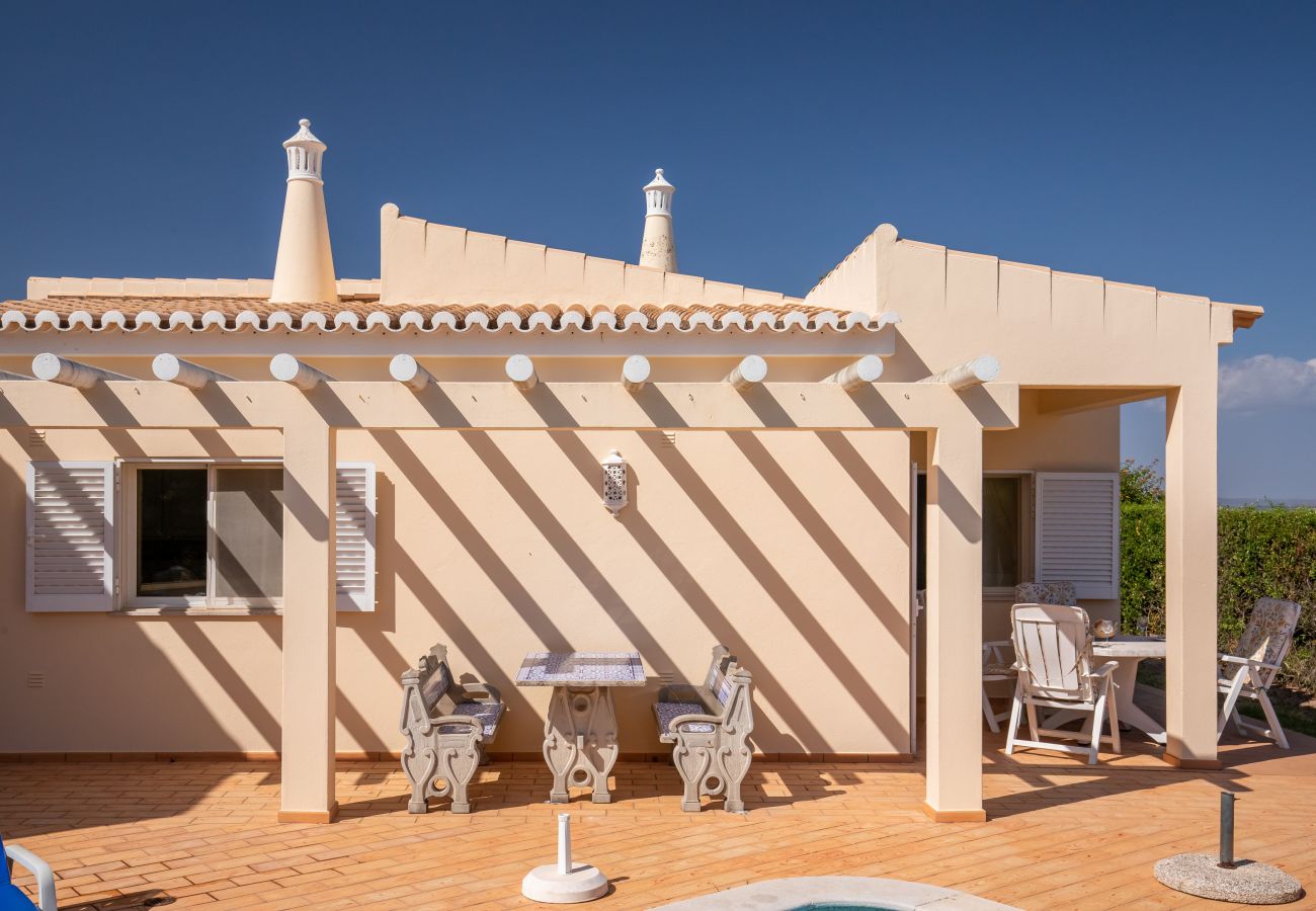 Überdachte Terrasse mit Essbereich und Poolblick. Sonnige Terrasse mit zwei gedeckten Tischen und Pergola vor einem Ferienhaus mit Poolblick.