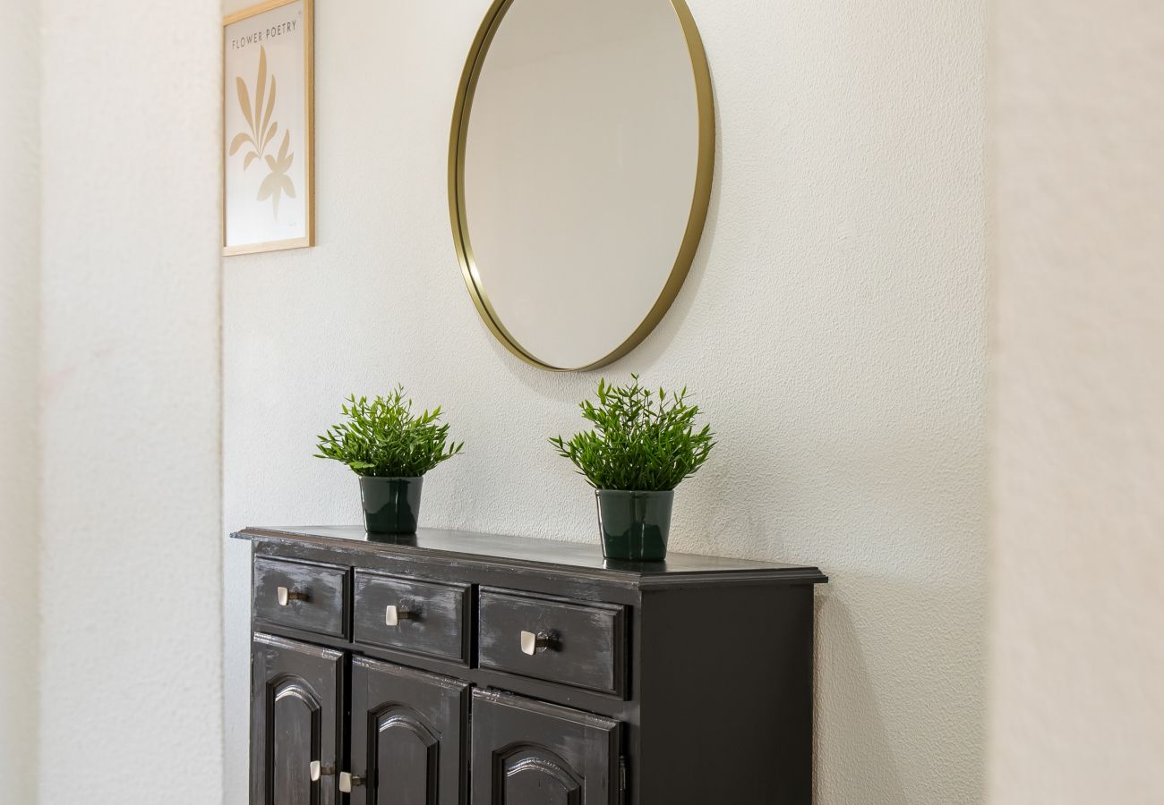 Eleganter Flur mit Dunklem Schrank und Goldspiegel Dunkelbrauner Holzschrank mit zwei Pflanzen, darüber ein runder Goldspiegel, in einem hellen Flur.