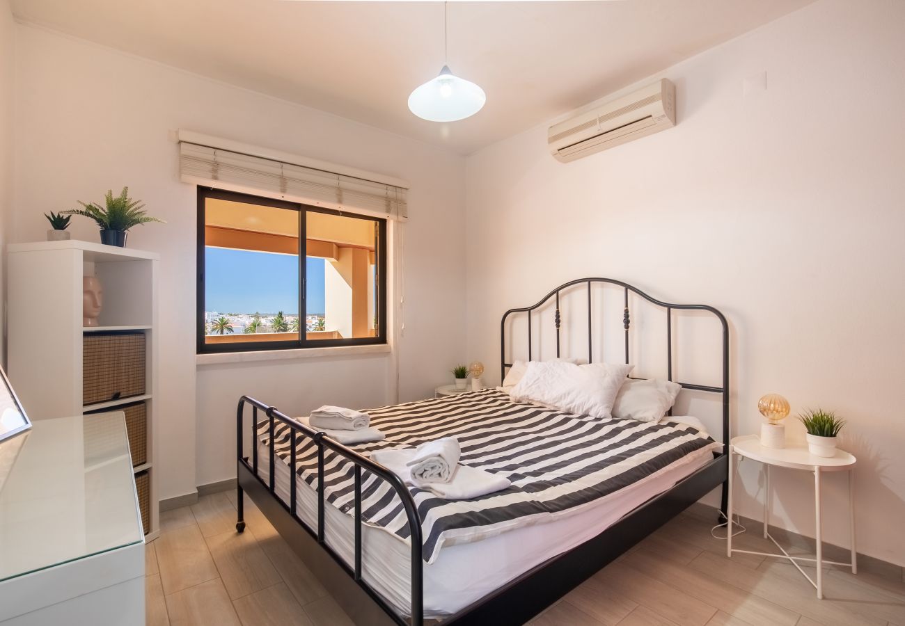 Helles Schlafzimmer mit Streifen-Design und Ausblick Schlafzimmer mit schwarzem Metallbett, gestreifter Bettwäsche, weißem Regal und Fenster mit sonnigem Blick nach draußen.