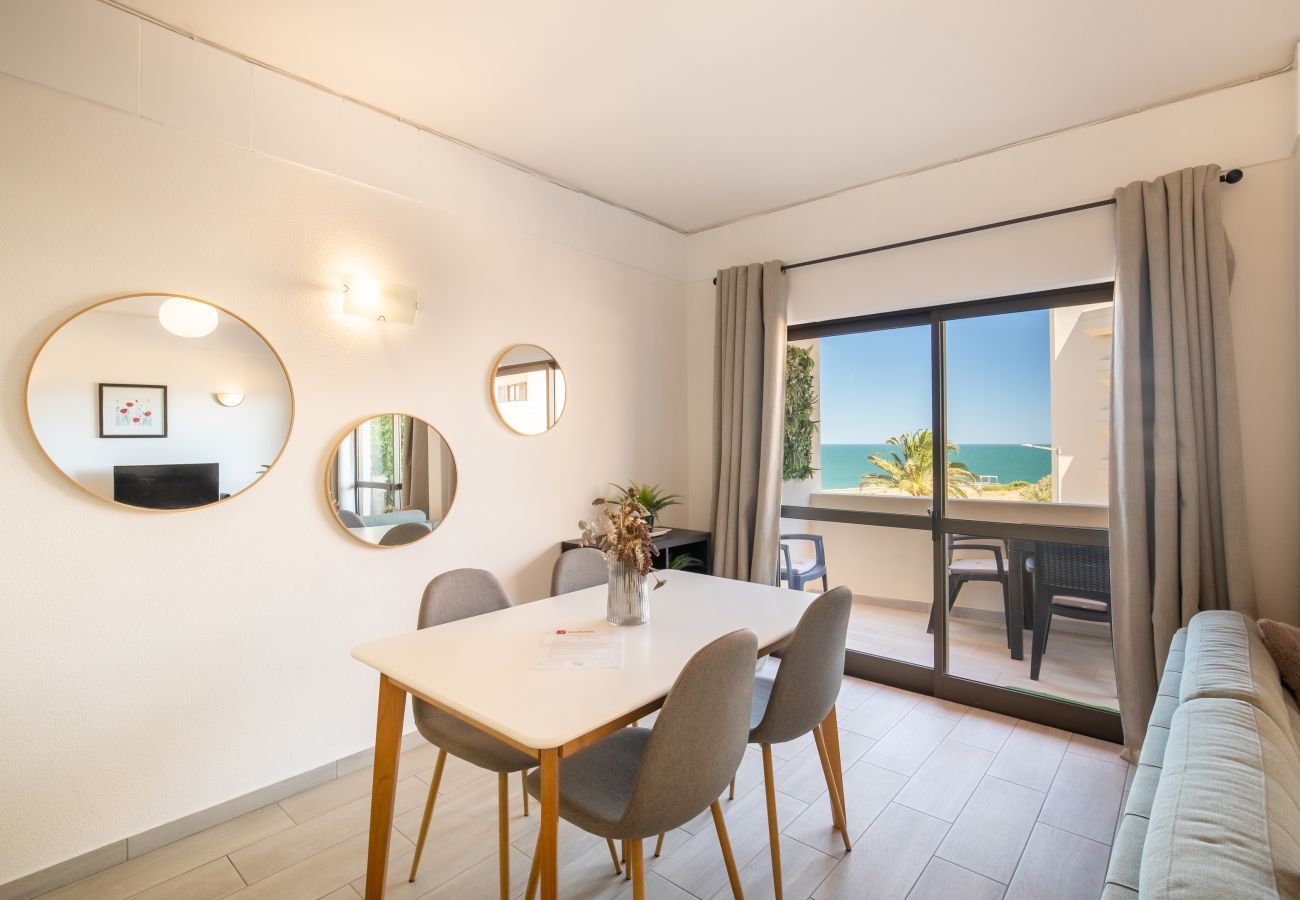 Stilvoller Essbereich mit Meerblick und Gold-Akzenten Heller Essbereich mit weißem Tisch, grauen Stühlen, runden Spiegeln und einem großen Fenster mit Meerblick.