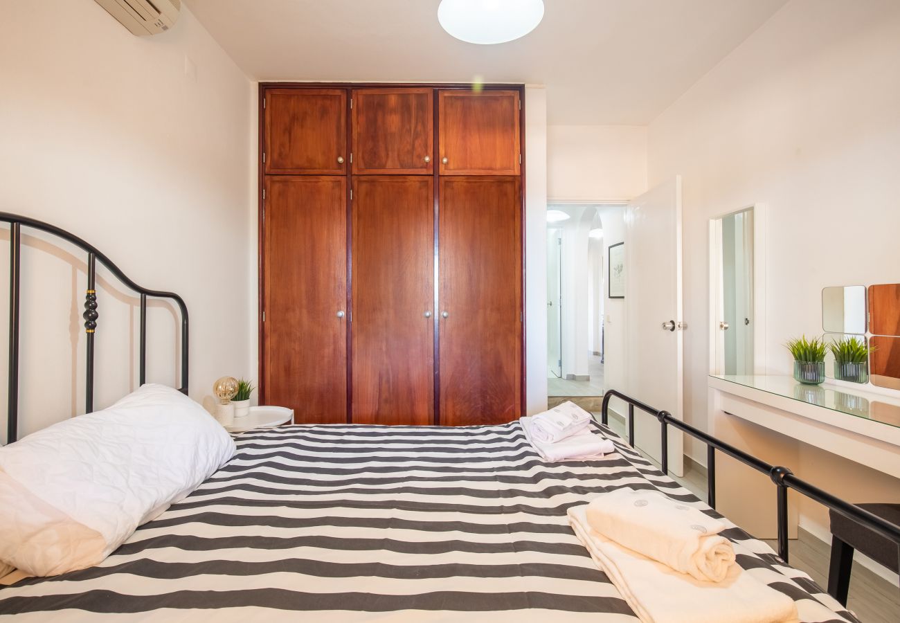 Gemütliches Schlafzimmer mit Holzschrank und Streifen Blick auf ein Doppelbett mit gestreifter Decke, Holzschrank, Schminktisch und geöffneter Tür im Schlafzimmer.